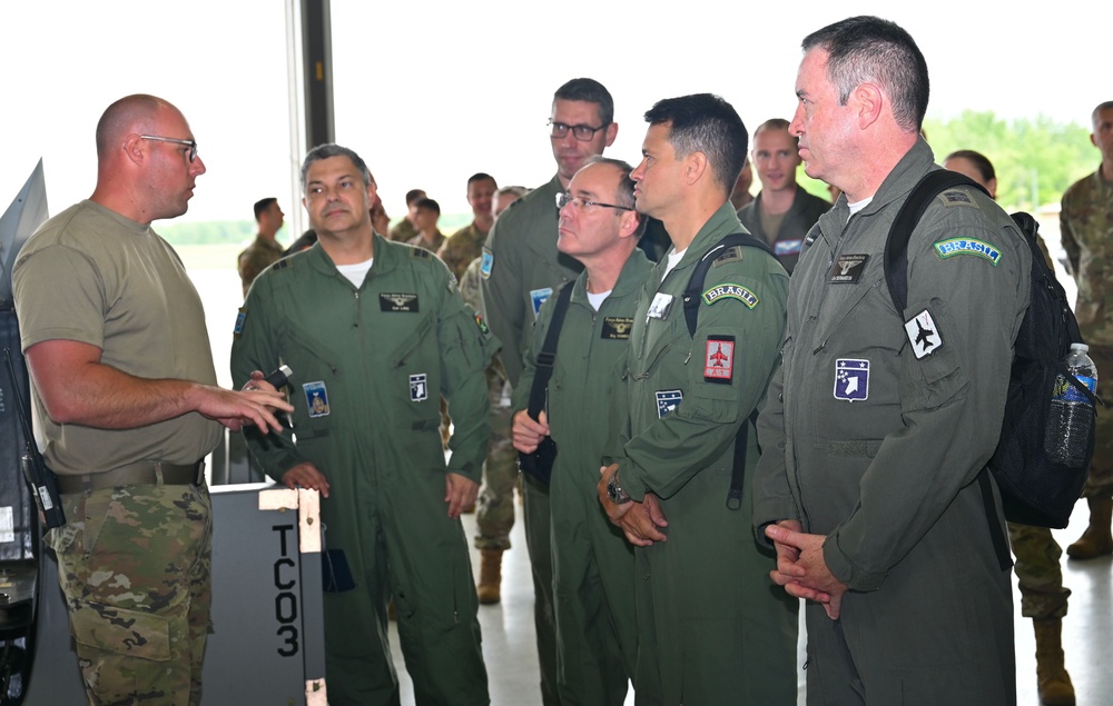 
                New York Air National Guard Master Sgt. Eric Wintersteen, a crew chief assigned to the 174th  Attak Wing's Maintenance Group, explains the airframe and engine inspection he is performing on an MQ-9 Repear remotely piloted aircraft to   Brazilian Air  Force officers  visiting  Hancock Field Air National Guard Base, in Syracuse, New York, on June 6, 2022. The Hancock Field stop was part of a week-long tour of New York Air National Guard facilities the Brazilian team of eight officers and NCOs was conducting as part of the  State Partnership Program. (U.S. Air ational Guard photo by Master Sgt. Barbara Olney)            
