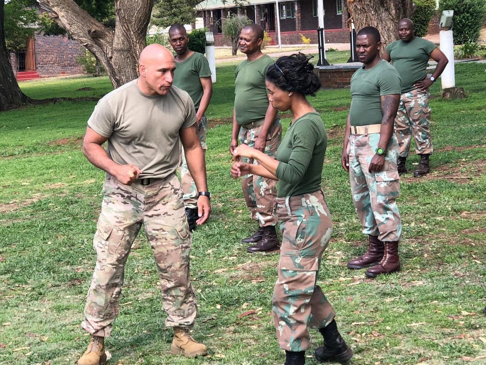 
                New York Army National Guard Master Sgt. Luis Barsallo, a certified hand-to-hand tactics instructor, demonstrates a move to members of the South African National Defense Forces during an  exchange visit on October 10, 2018. Soldiers from the New York Army National Guard took  part in an exchange program at the South African National Defense Forces Military Police School during an exchange visit there on Oct. 10-11, 2018. Twelve New York Army National Guard experts in civil support operations, military police, law enforcement, and self-defense took part in the exchange visit. ( U.S. Army National Guard photo by Sgt. Kristin Ross)            